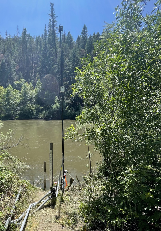 Hyperspectral sensor installed at Requa on the lower Klamath River — sensor pole beside murky brown river water in dense forest